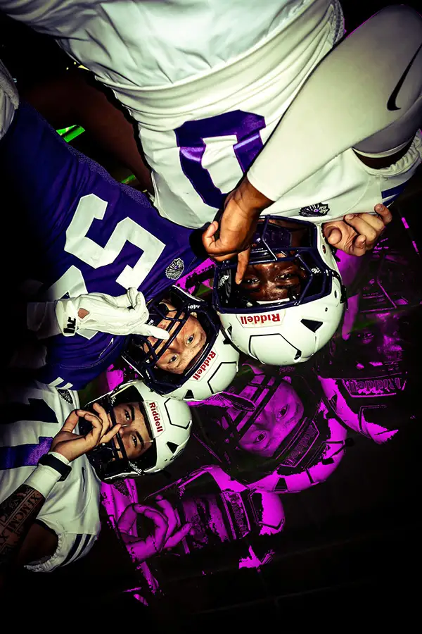 Football players in helmets looking down into the camera, edited in purple and magenta