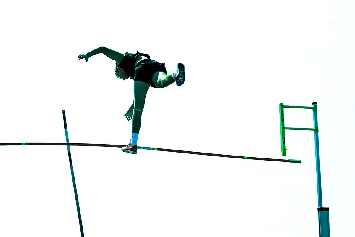 Pole vaulter silhouetted over the bar against a white sky