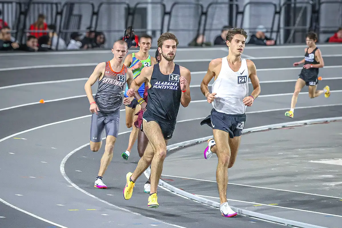 Pack of distance runners leaning into the curve of an indoor track