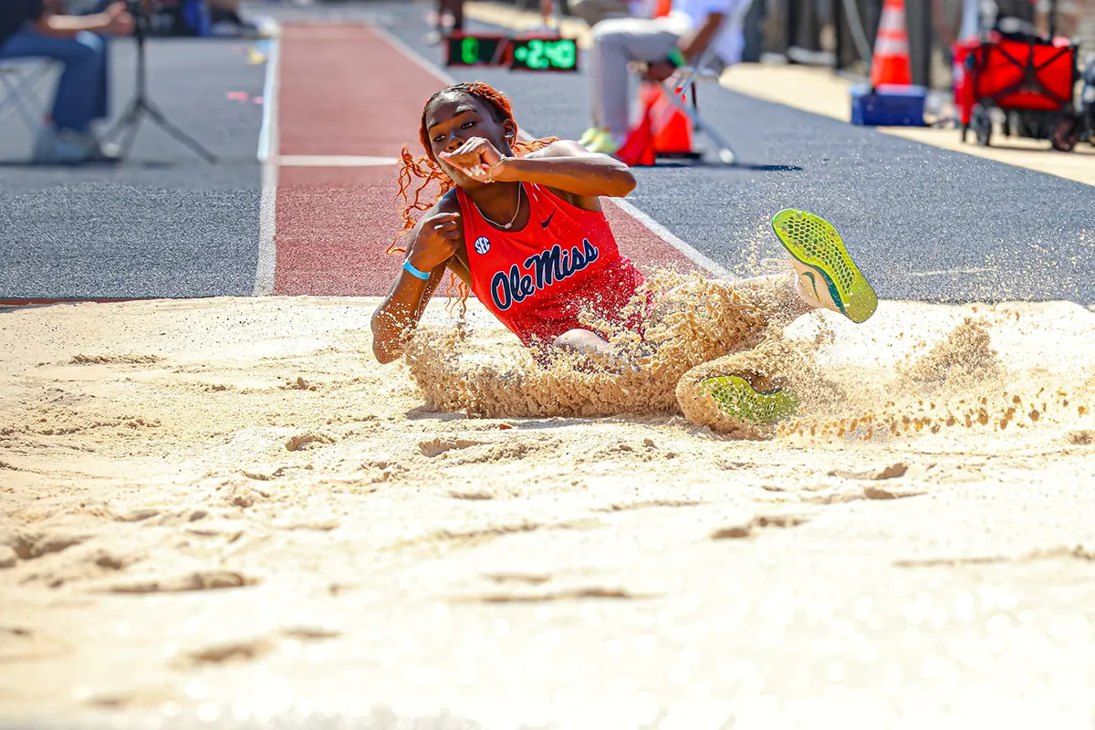 Long jumper in an Ole Miss uniform landing in a spray of sand