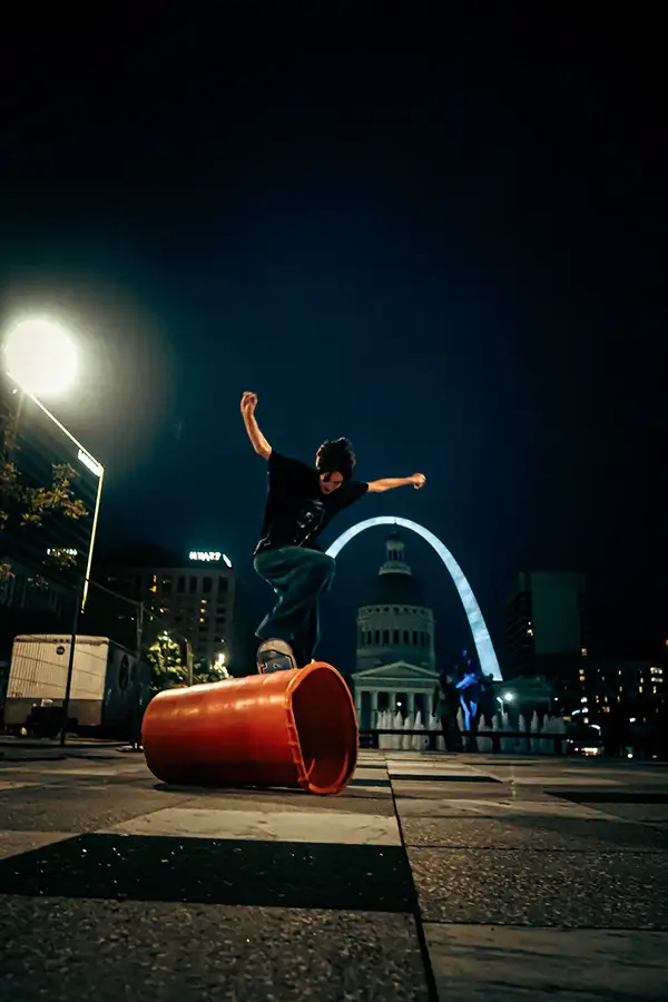 Skateboarder in the air at night with the Gateway Arch lit behind