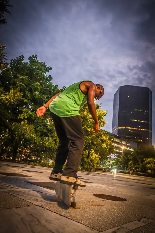 Skateboarder riding past downtown towers at dusk