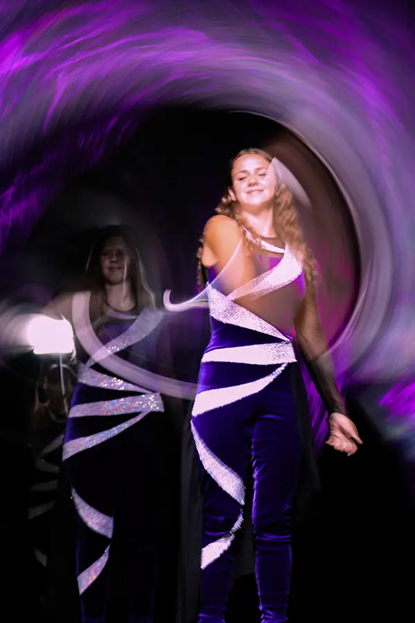 Dancer in purple and white swirled by a purple light tunnel