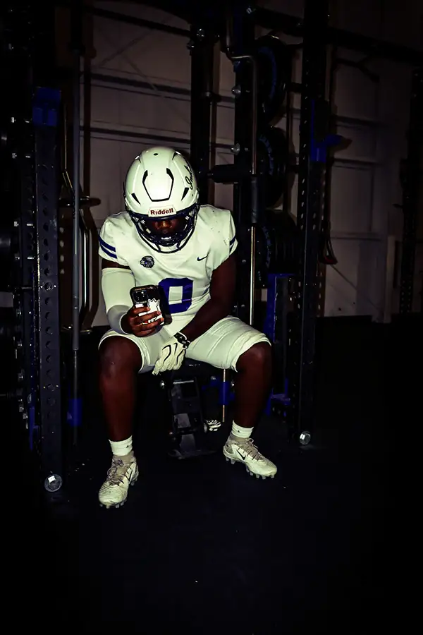 Football player in white sitting in a dark weight room