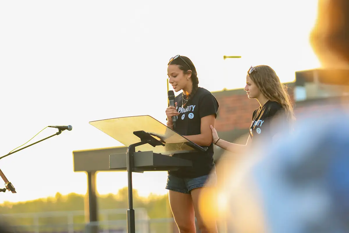 Two students speaking at a podium outdoors at golden hour