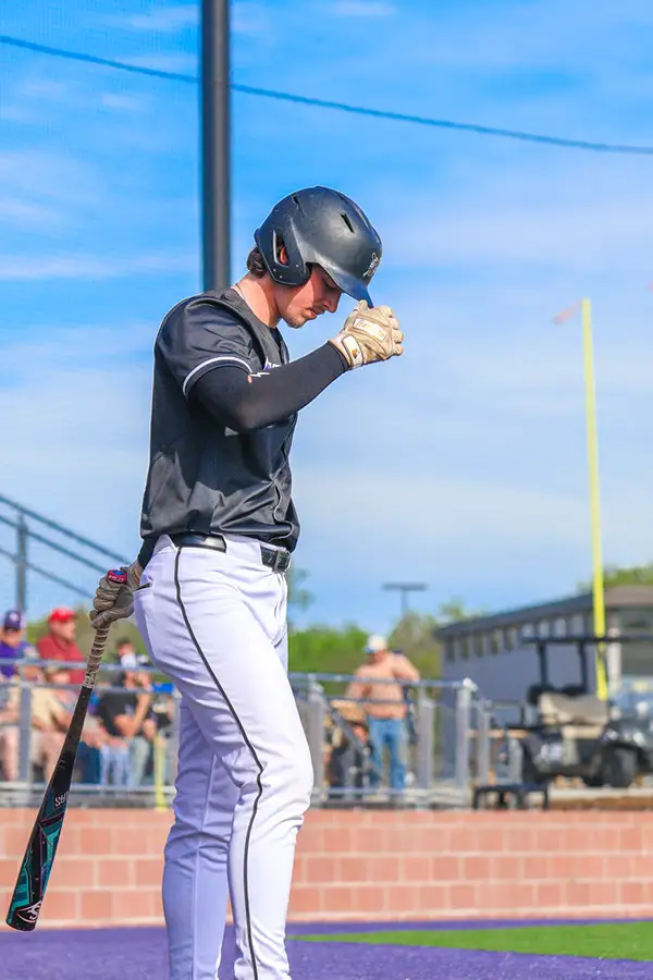 Batter adjusting his helmet beside the dugout