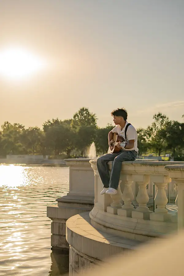 Young man with a guitar on a stone wall by the water