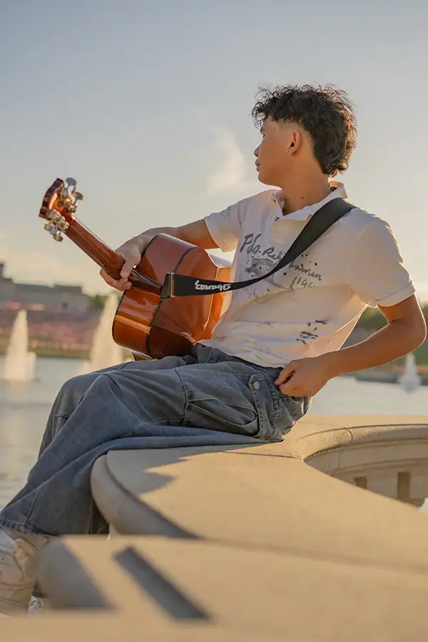 Young man playing guitar by a fountain at sunset