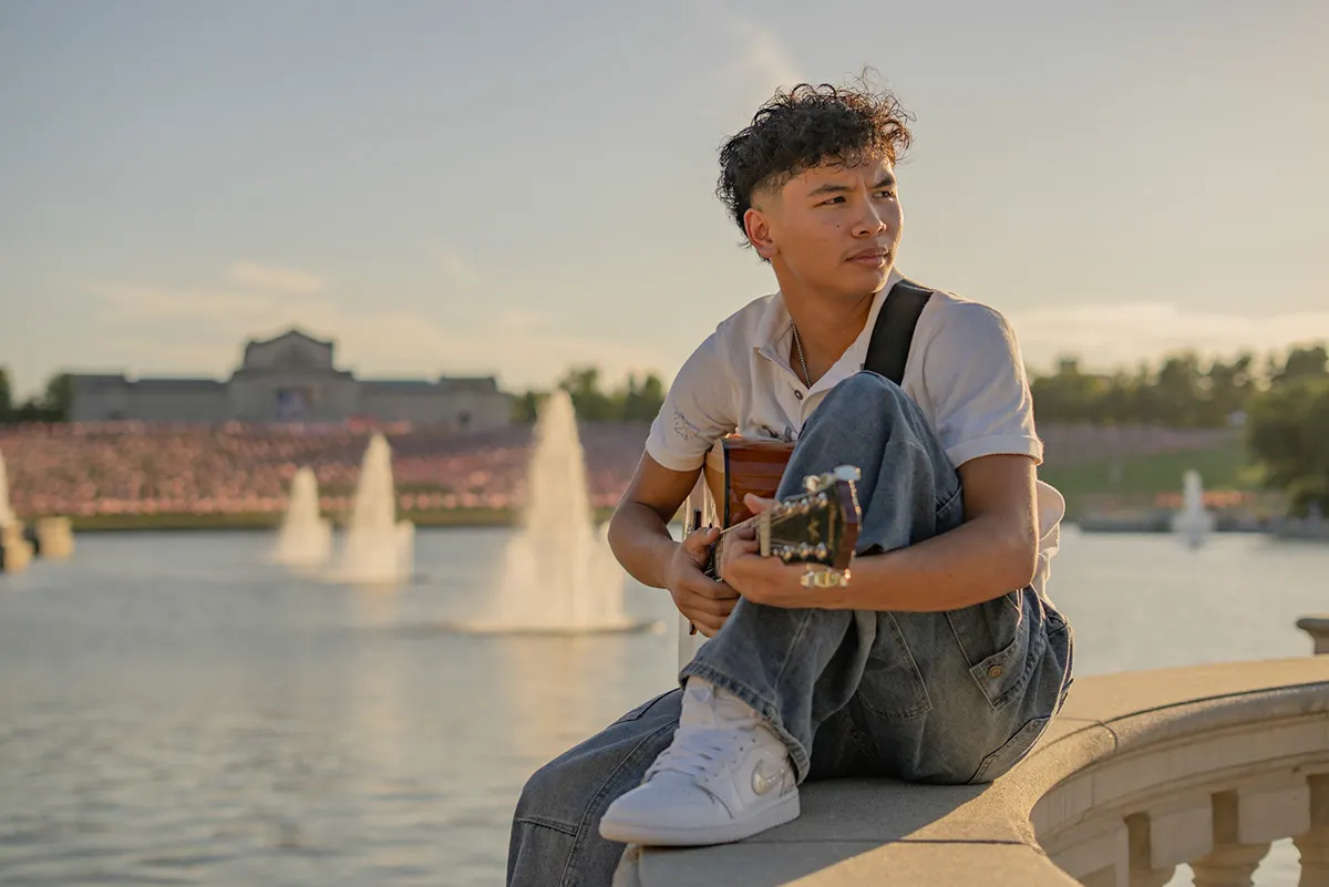 Young man with a guitar sitting by the fountains, looking out