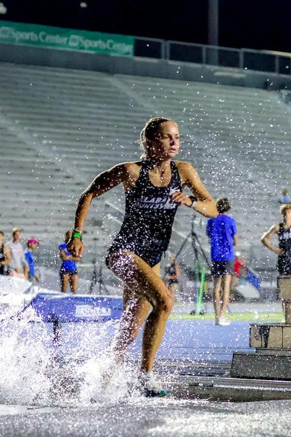 Steeplechase runner splashing through the water pit