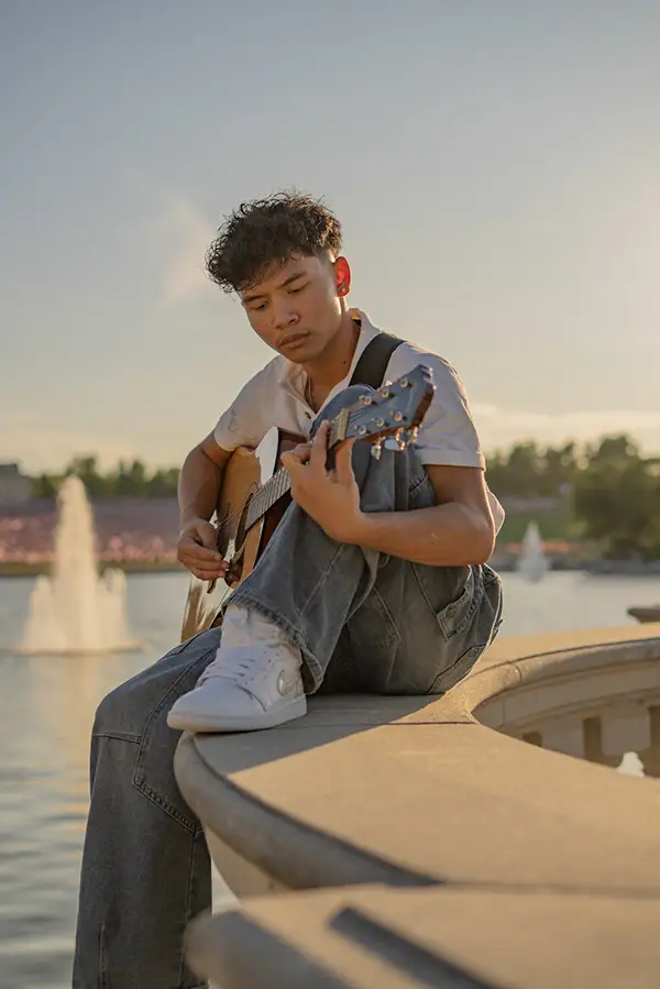 Young man strumming a guitar on the fountain's edge
