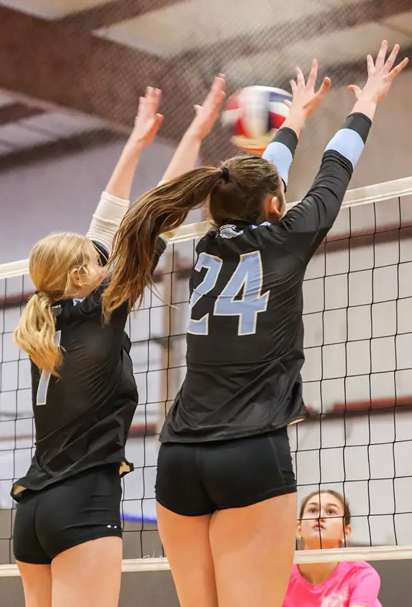 Two volleyball players leaping at the net to block