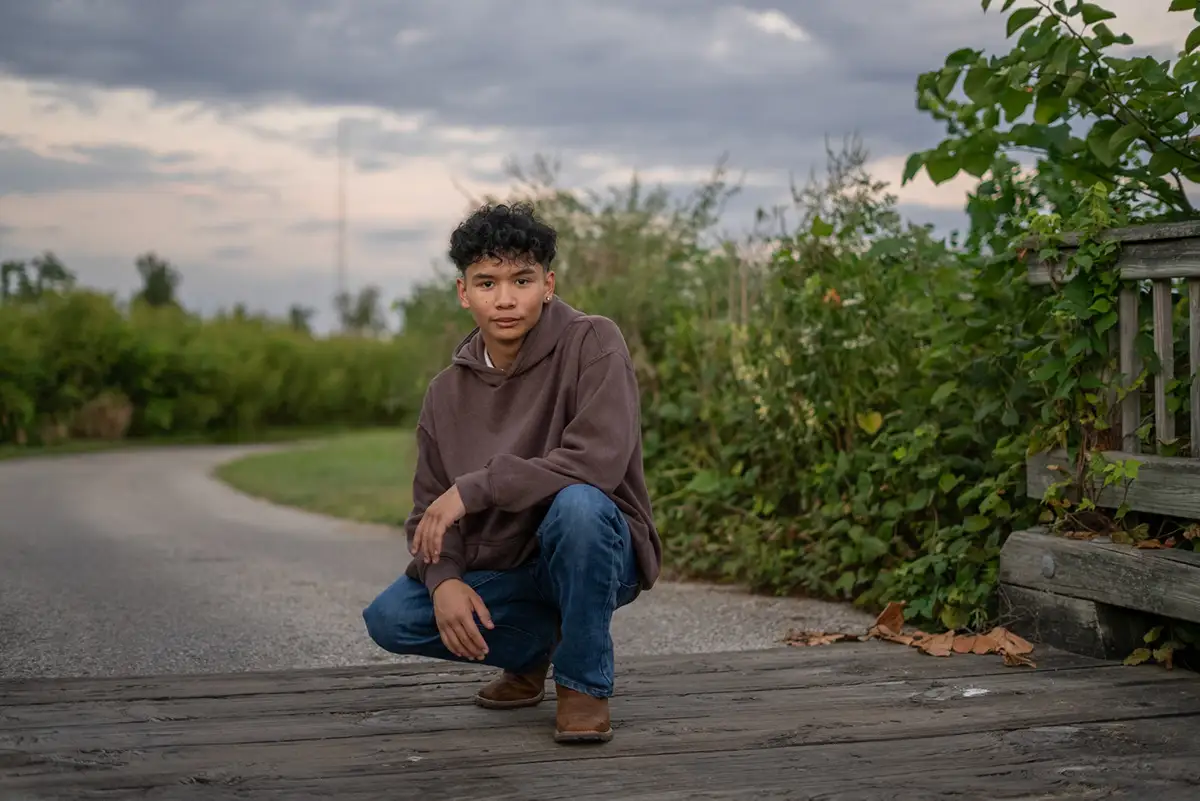 Young man crouching on a park path under a cloudy sky