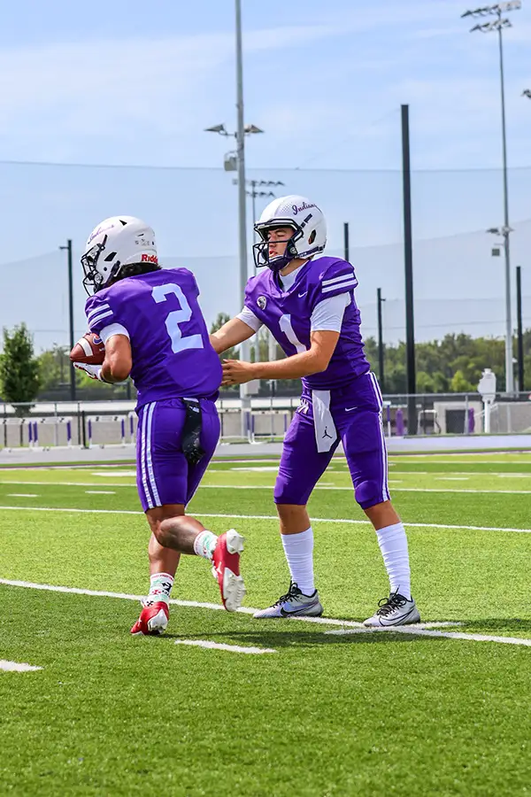 Two football players in purple slapping hands on the field